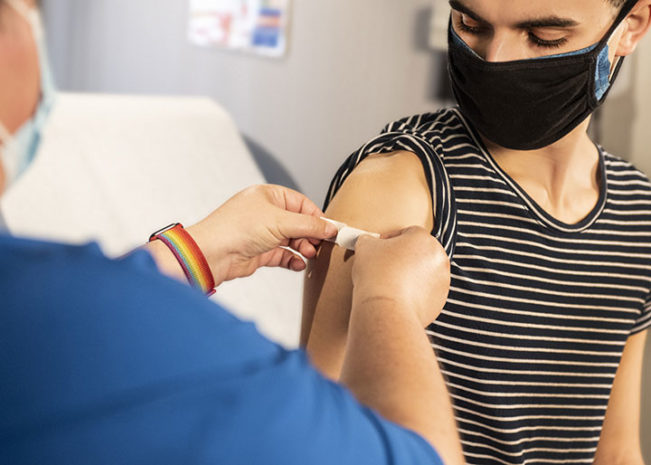 Man in striped shirt with mask getting bandage after vaccine shot